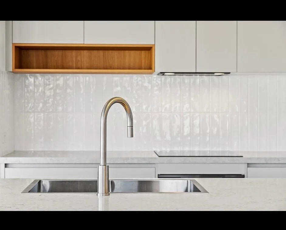 Modern kitchen sink with marble countertop and white cabinets.