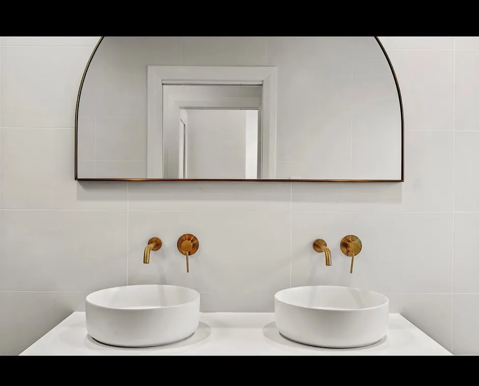 Modern bathroom with double sinks and round gold faucets.