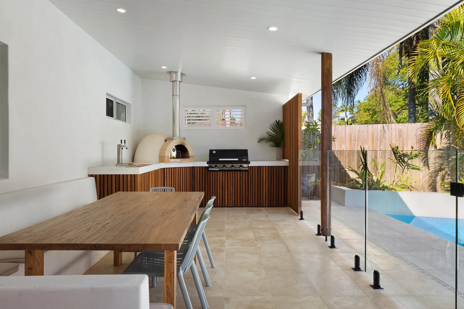 Outdoor kitchen with dining area next to a pool.